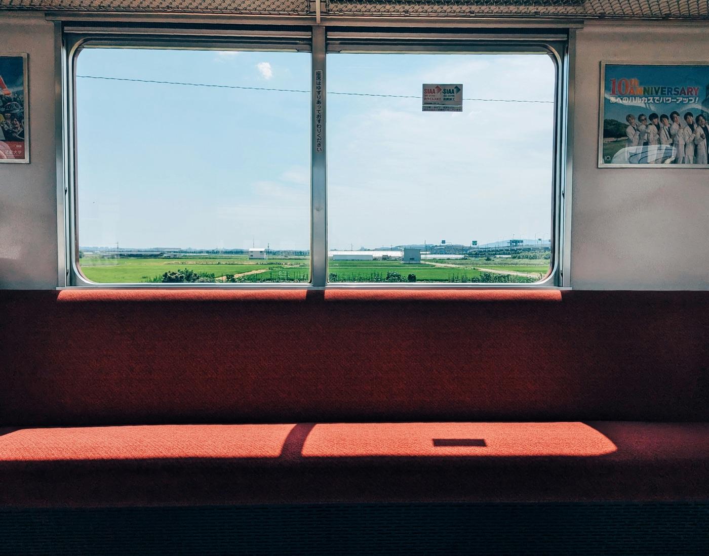 赤い座席と、窓の外に田園が広がる近鉄電車の車内