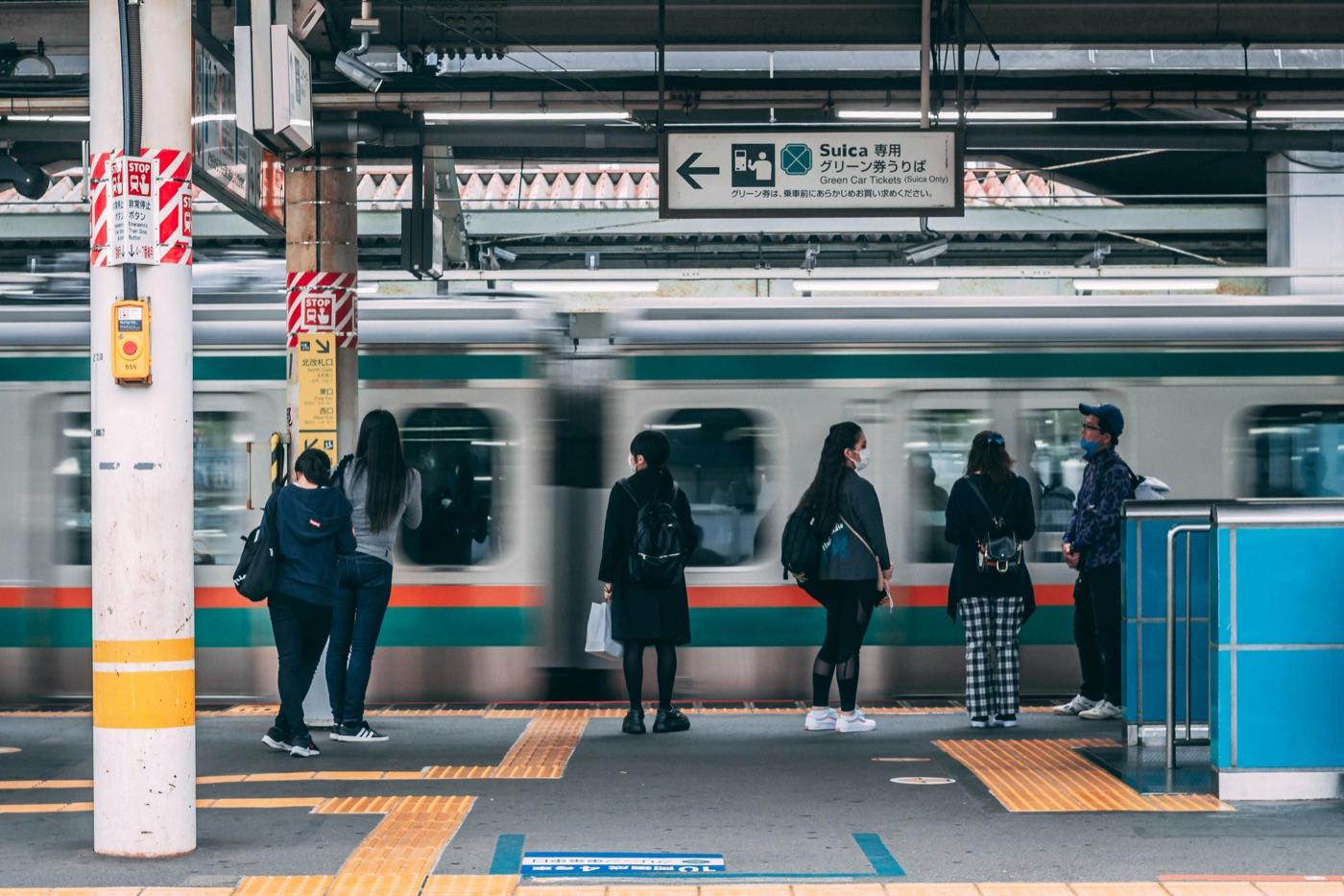 JRのホームで電車を待つ人たちの後ろ姿。頭上にSuica専用グリーン券売り場の案内