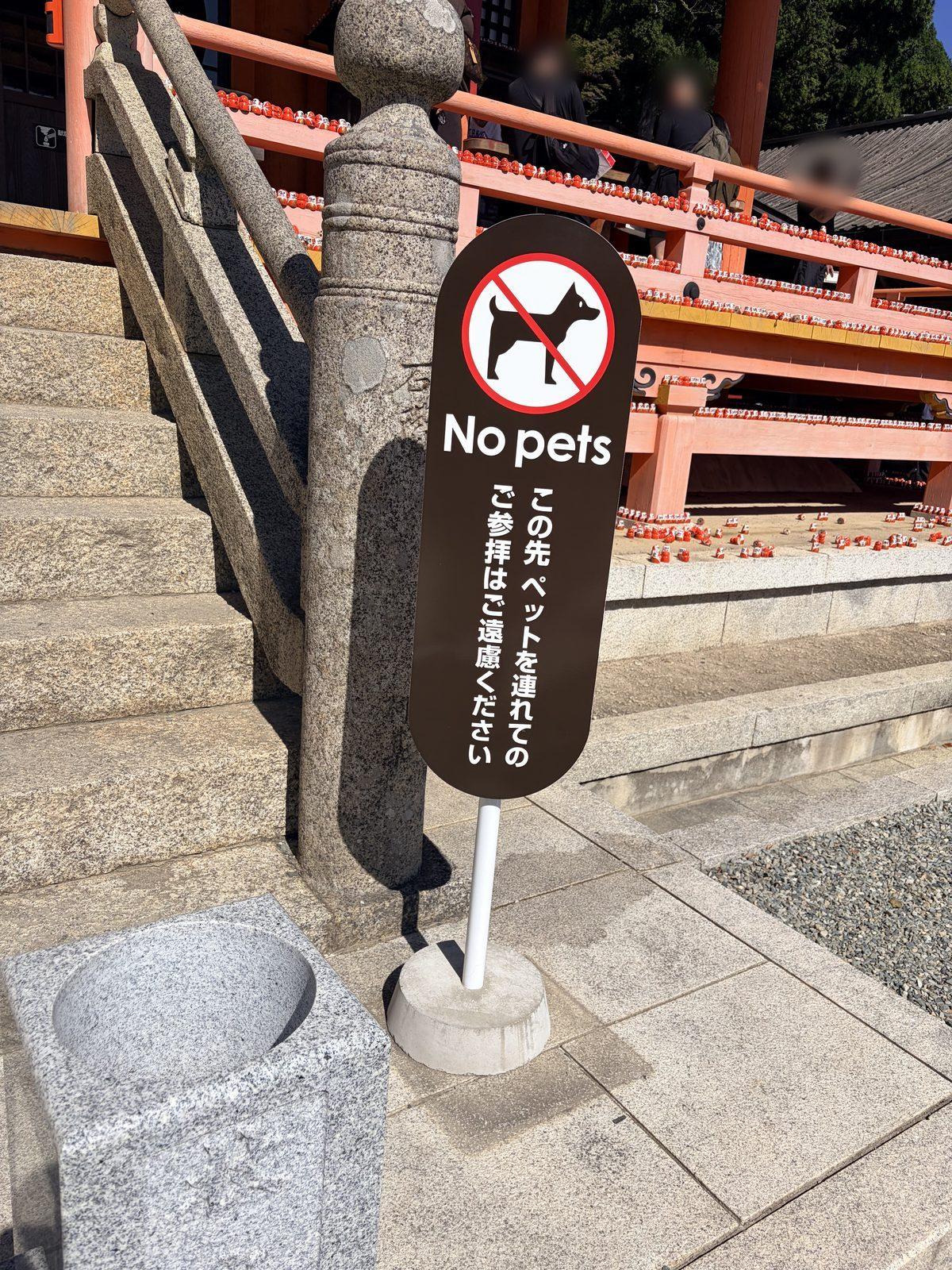 朱色の本堂へ上がる石段の手前に立つ、「No pets」の札。犬に斜線のマークと、この先はペットを連れての参拝を遠慮してほしいという文が書かれている