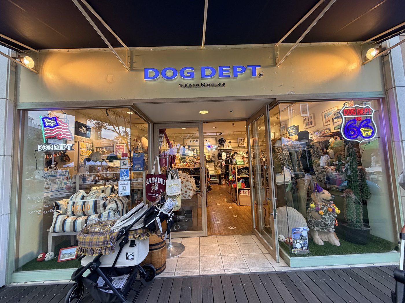 「DOG DEPT」の看板が出たお店の入口。ガラスのウインドウには犬用のベッドやクッションが並び、店先にはペットカートが1台とまっている