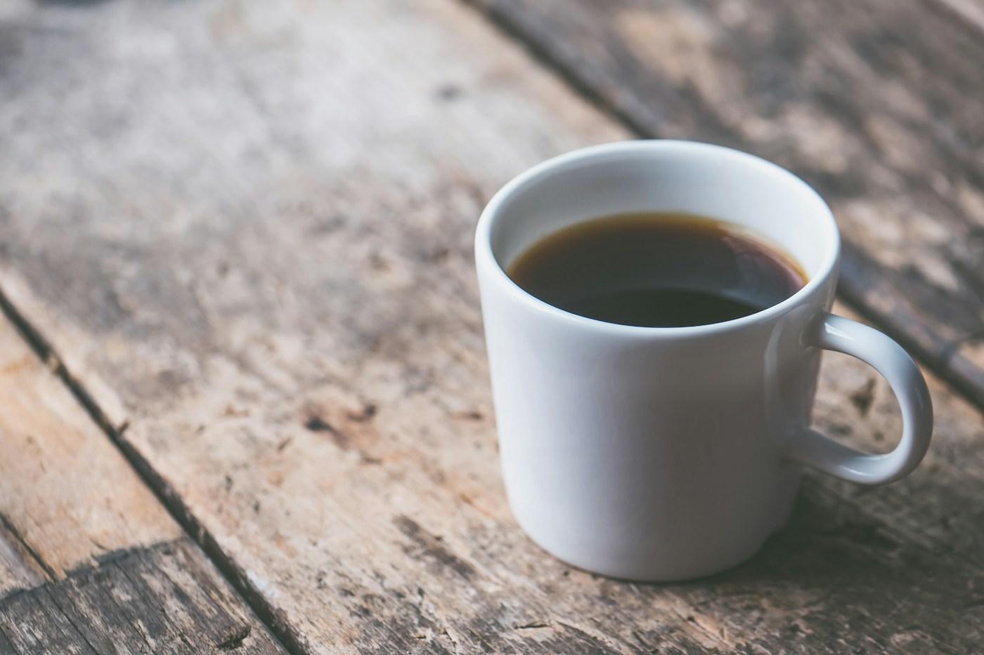 木のテーブルに置かれた、コーヒーの入った白いマグカップ