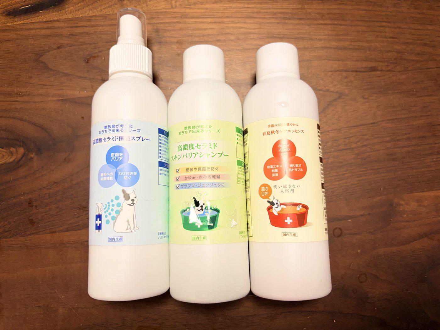 木のテーブルに並んだ、保湿スプレー・シャンプー・入浴剤の白いボトル3本